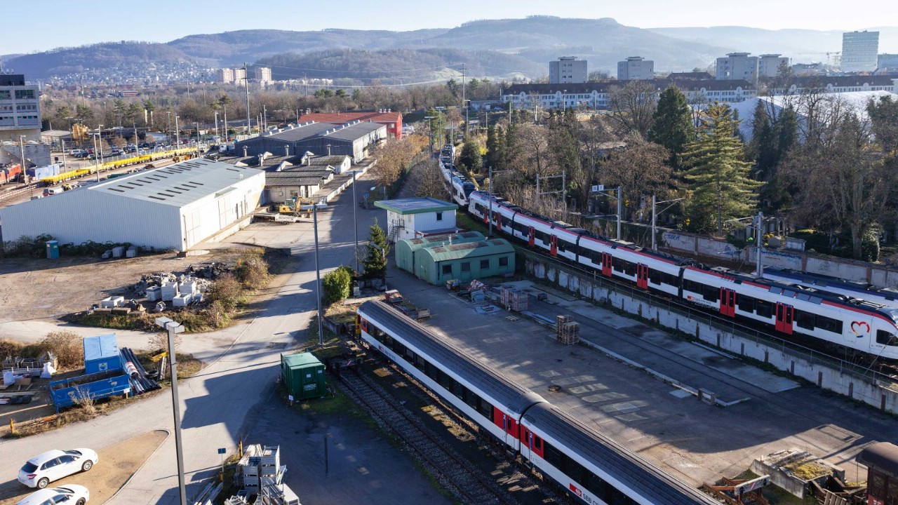 Das Bild zeigt Abstellgleise mit Zügen, Lagerhallen und einen Weg.