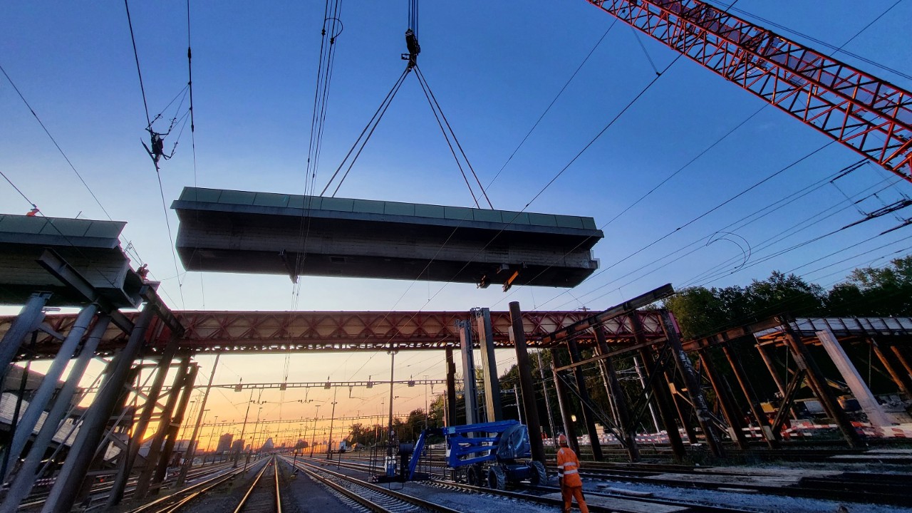 Ein grosser Kran hebt bei abendlicher Stimmung ein grosses Brückenelement der alten Brücke über den Gleisen des Rangierbahnhofs aus. 